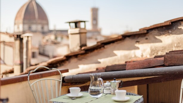 A table with a pitcher, cups, and a teapot on a balcony overlooking a historic dome and tower.