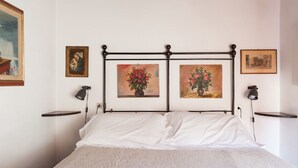 A neatly made bed with white linens, a metal headboard, and two wall-mounted lamps.