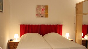 A hotel room with two beds, red curtains, a wooden nightstand with a lamp, and a painting on the wall. - studio - Bonifacio (Bonifacio)
