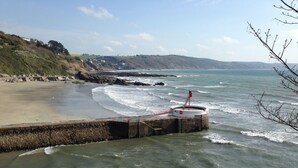 A coastal scene with a stone pier extending into the sea, a lighthouse on the pier, and a sandy beach with a rocky cliff in the background. - Lovely Flat In West Looe With Spectacular Sea & Harbour Views - Non Smokers Only (Looe)