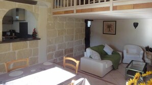 Una sala de estar acogedora con una pared de piedra, una mesa de comedor, un sofá y un balcón con barandas blancas.