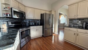 A modern kitchen with stainless steel appliances, white cabinetry, and a black granite countertop. - 🏡 7 Bed,7 Bath | Large pool & H/Tub | Large Smart TVs & Sonos every Room I WiFi (Davenport)