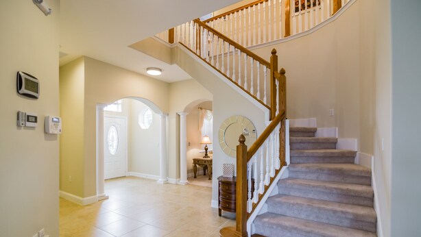 A spacious foyer with a grand staircase, a clock, and a door leading to another room. - 🏡 7 Bed,7 Bath | Large pool & H/Tub | Large Smart TVs & Sonos every Room I WiFi (Davenport)