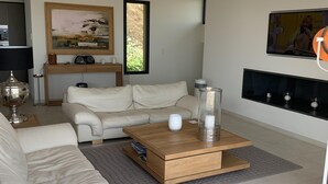 A modern living room with a white leather sofa, a wooden coffee table, and a TV mounted on the wall. - Villa with breathtaking views of Pinarello bay and beach (Zonza)