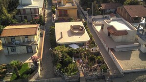 An aerial view of a coastal area with buildings, a sandy beach, and a small garden area with palm trees.