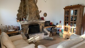 A living room with a stone fireplace, white leather sofas, and a wooden cabinet with glass doors.