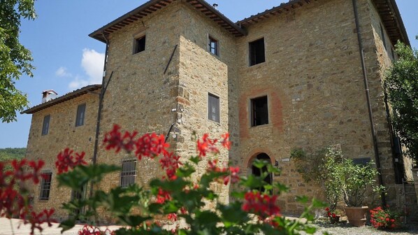 A stone building with multiple windows and a small garden area with red flowers.