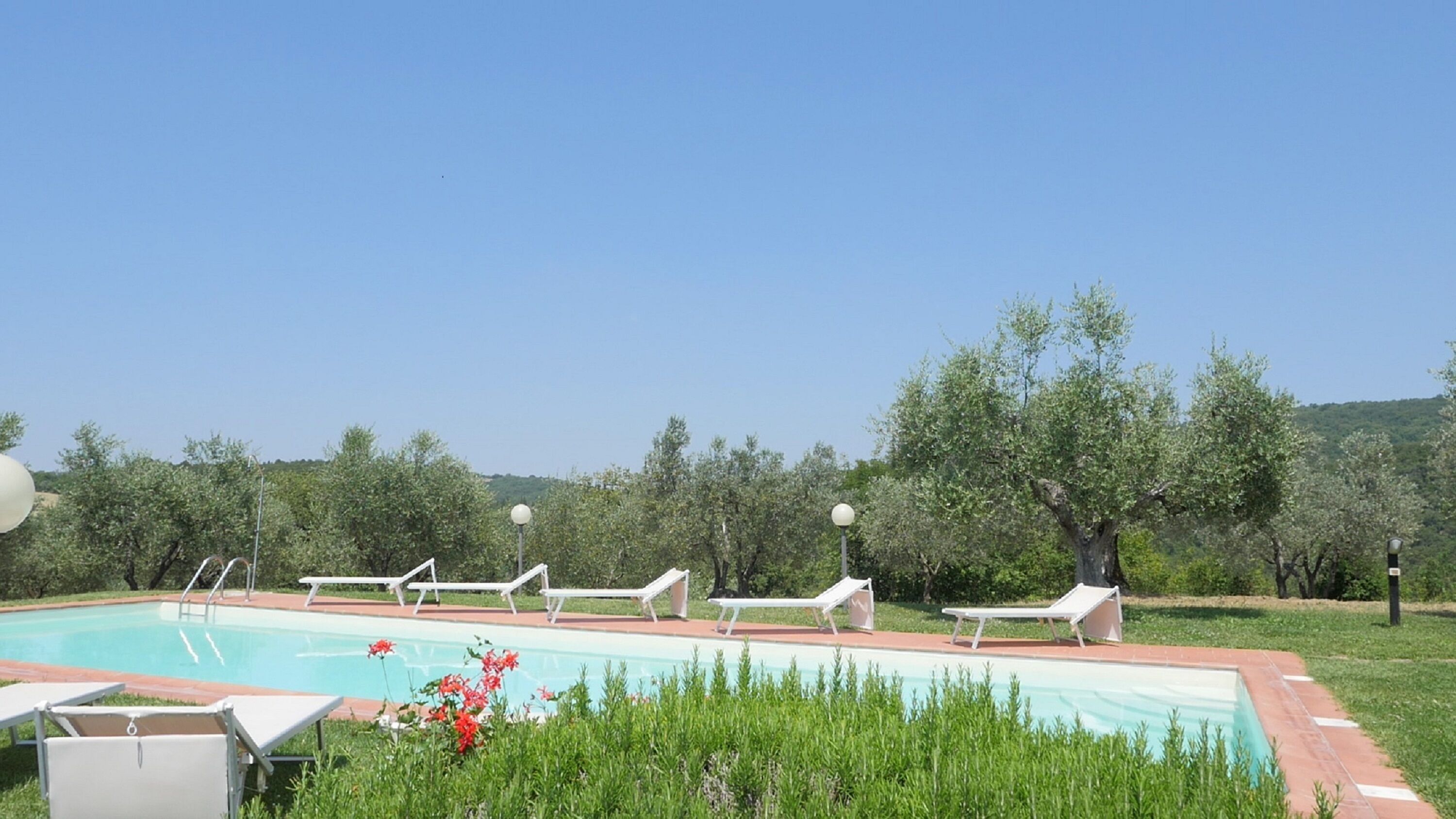 A swimming pool with lounge chairs and a clear view of trees and hills in the background.