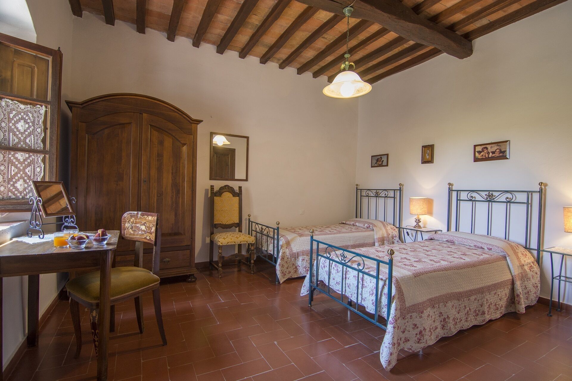 A traditional room with two beds, a wooden wardrobe, a desk with a chair, and a hanging light fixture.
