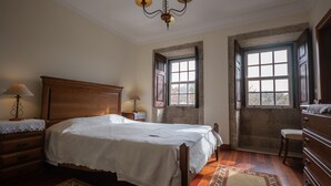 Een slaapkamer met een houten bed, twee bedlampen, een kroonluchter en een groot raam met uitzicht.
