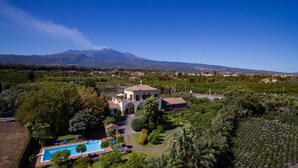 A villa with a swimming pool, surrounded by lush greenery and a view of a mountain.