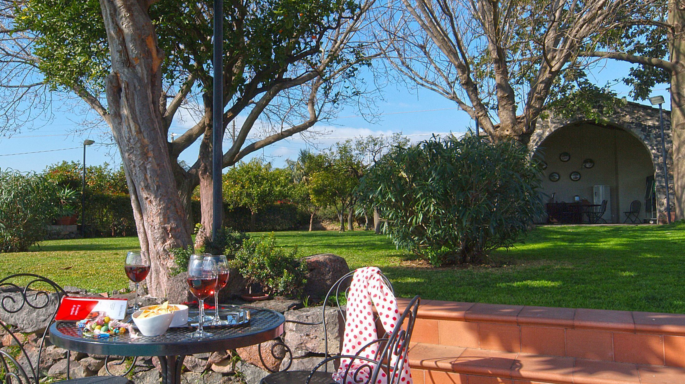 An outdoor dining area with a table set for two, surrounded by greenery and a stone wall.