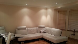 Un salon moderne avec un canapé d’angle, un fauteuil blanc et un plancher en bois.