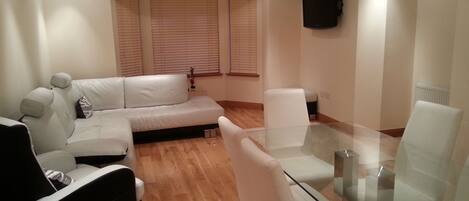 A modern living room with a sofa, a glass coffee table, and a TV mounted on the wall.