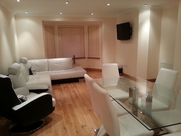 A modern living room with a sofa, a glass coffee table, and a TV mounted on the wall.