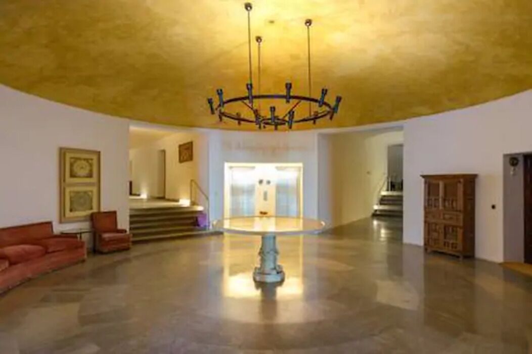 Un hall d’entrée spacieux, agrémenté d’un lustre central, d’un escalier menant à un étage supérieur et d’une armoire en bois.