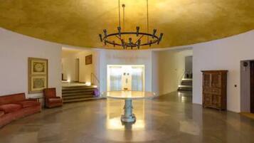 Un hall d’entrée spacieux, agrémenté d’un lustre central, d’un escalier menant à un étage supérieur et d’une armoire en bois.