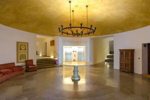 Un hall d’entrée spacieux, agrémenté d’un lustre central, d’un escalier menant à un étage supérieur et d’une armoire en bois.