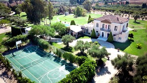 Una casa grande con cancha de tenis, rodeada de exuberante follaje y árboles.