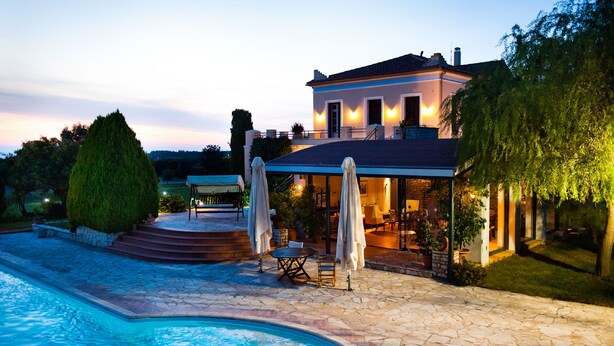 Una casa de dos pisos con piscina, zona de estar exterior y un porche cubierto.