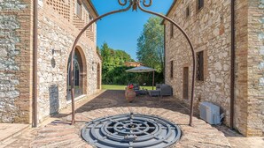 Un pati amb murs de pedra, una estructura circular metàl·lica al centre, mobles d'exterior i un parasol gran.