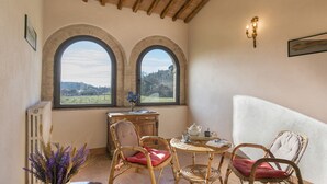 Habitació acollidora amb dues finestres d'arc que donen vista al camp, una taula petita amb cadires i un radiador a la paret.
