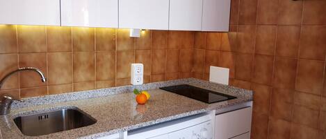 Una cocina con encimera de granito, pileta de acero inoxidable y cocina eléctrica integrada.