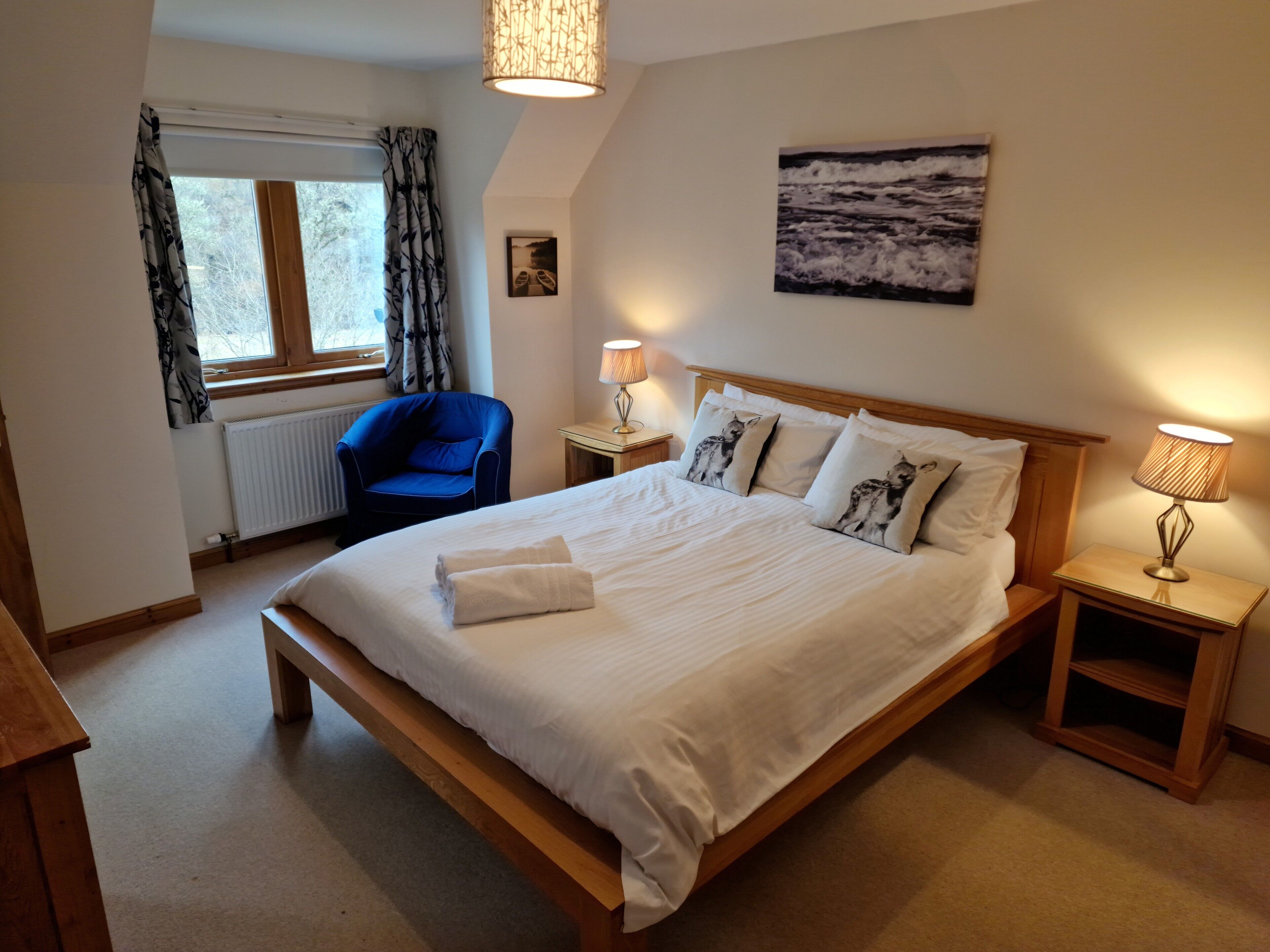 A neatly arranged bedroom with a large bed, a chair, a lamp, and a window with curtains.