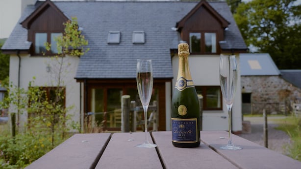 A bottle of champagne and two glasses on a wooden table with a house in the background. - Shepherds Rest self catering sleeps 6, pets welcome. (Fort William)