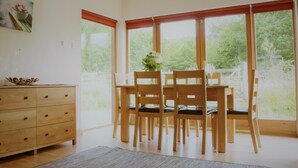 A dining area with wooden chairs and a table, large windows with red blinds, and a wooden cabinet with drawers. - Shepherds Rest self catering sleeps 6, pets welcome. (Fort William)