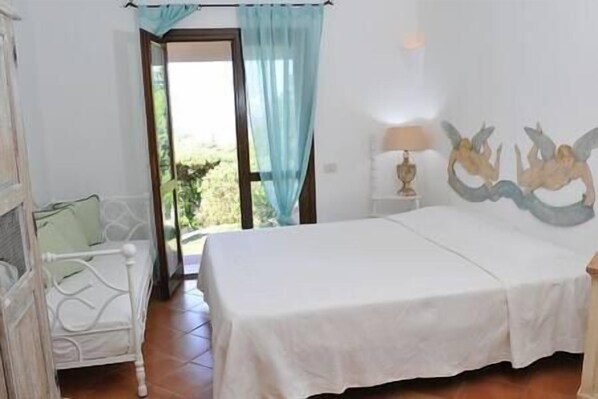 A bedroom with a bed, a nightstand, a lamp, and a window with curtains. - Porto Rafael, wonderful villa 3 rooms e 3 bathroom (Punta Sardegna)