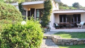 Una villa con un porche cubierto, mobiliario exterior y un camino de piedra que conduce a la entrada.