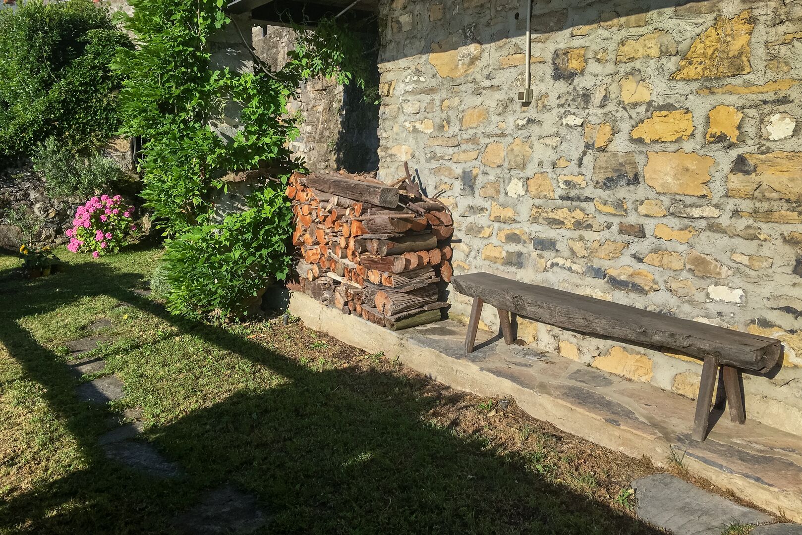 Un mur de pierres avec un banc en bois et une pile de bois de chauffage.