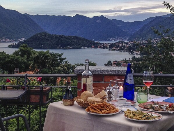 Une table dressée avec de la nourriture et des boissons, offrant une vue sur un paysage montagneux et une étendue d’eau.