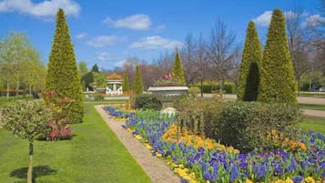 A formal garden with neatly trimmed hedges, a central fountain, and a variety of colorful flowers.