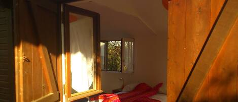 A bedroom with a bed, a window, and a mirror reflecting the outside view.