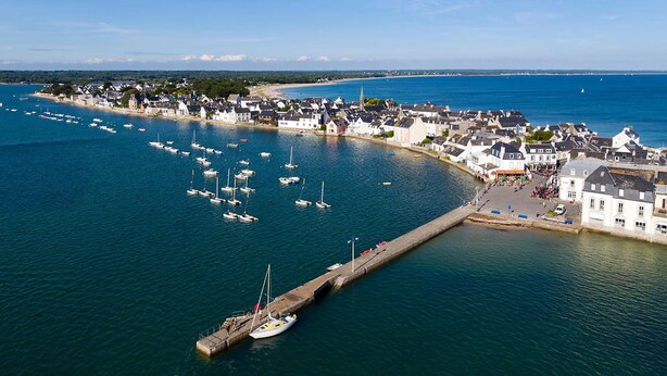 A coastal town with a marina filled with boats, a pier, and buildings along the waterfront.