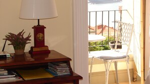 Ein Zimmer mit Schreibtisch, Lampe und Stuhl, einer kleinen Topfpflanze und einem Balkon mit Blick auf ein Kreuzfahrtschiff.
