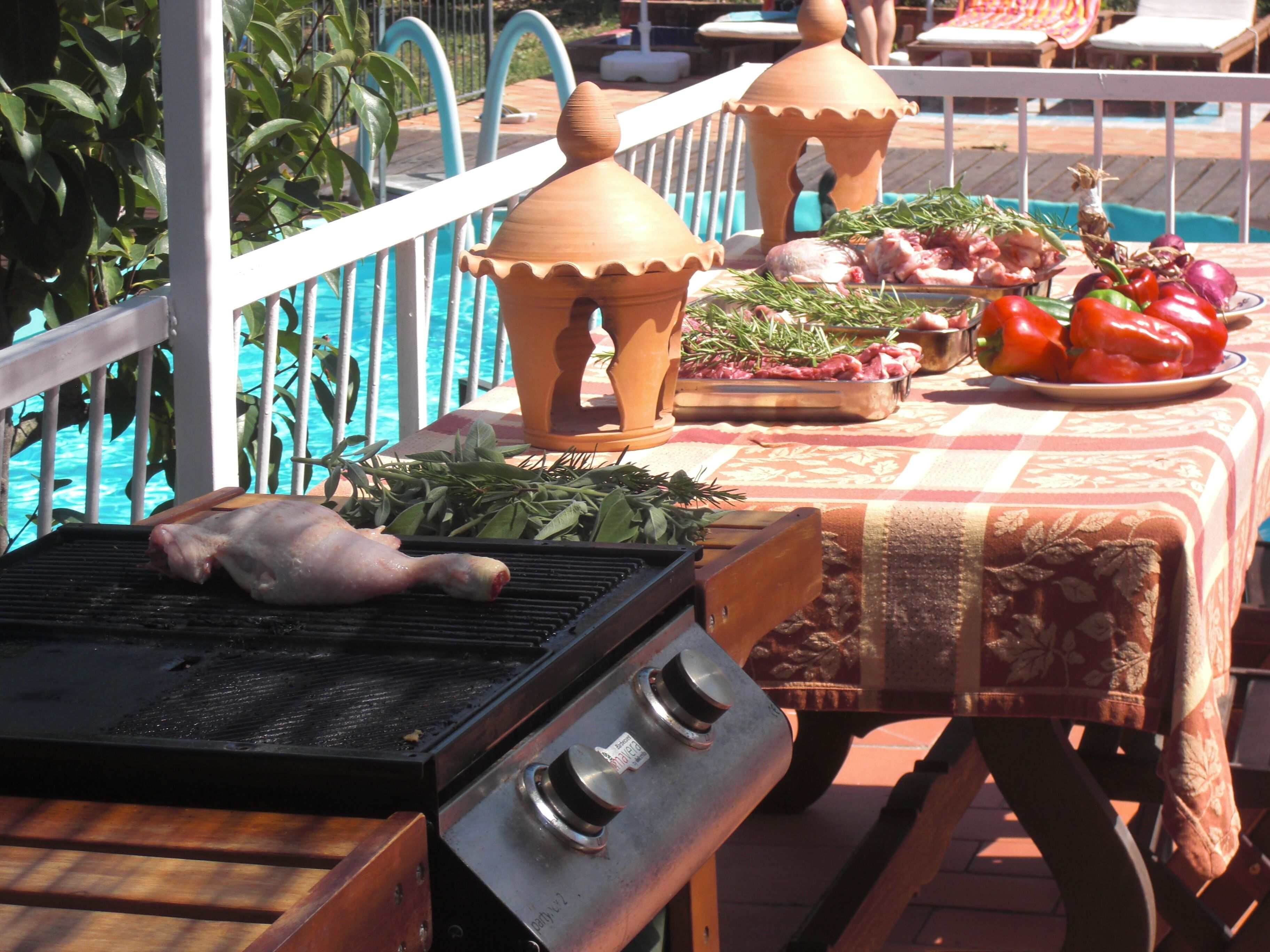 A barbecue grill with raw chicken and vegetables on a table near a pool.