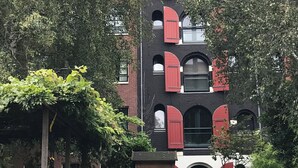 Un edificio de varios pisos con contraventanas rojas, rodeado de árboles y vegetación.