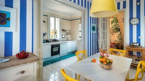 A kitchen with a blue and white striped backsplash, a yellow pendant light, and a dining area with a white table and yellow chairs. - Waterfront villa with panoramic terrace and garden (Fontane Bianche)