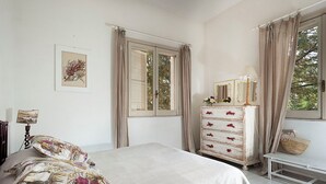 A bedroom with a bed, a dresser, a lamp, and a window with curtains. - Waterfront villa with panoramic terrace and garden (Fontane Bianche)