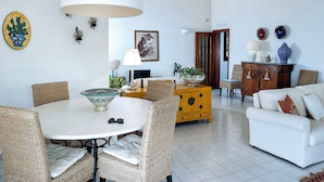 A living room with a round table, wicker chairs, a sofa, a yellow cabinet, and a white lamp. - Waterfront villa with panoramic terrace and garden (Fontane Bianche)
