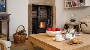 Un salón acogedor con chimenea, una mesa de madera con una cesta, manzanas, naranjas, una taza, un plato bajo y un plato con pasteles.