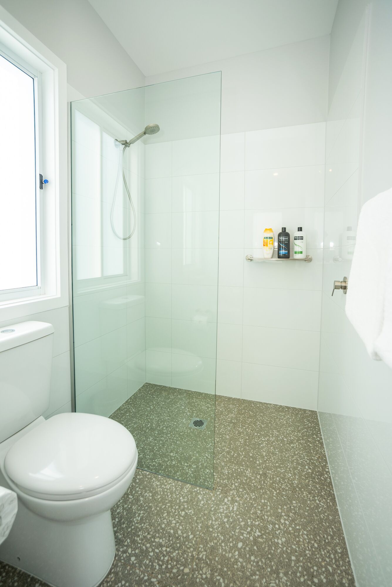 Ein modernes Badezimmer mit einer gläsernen Dusche, einer weißen Toilette und einem Ablagefach mit Pflegeartikeln.
