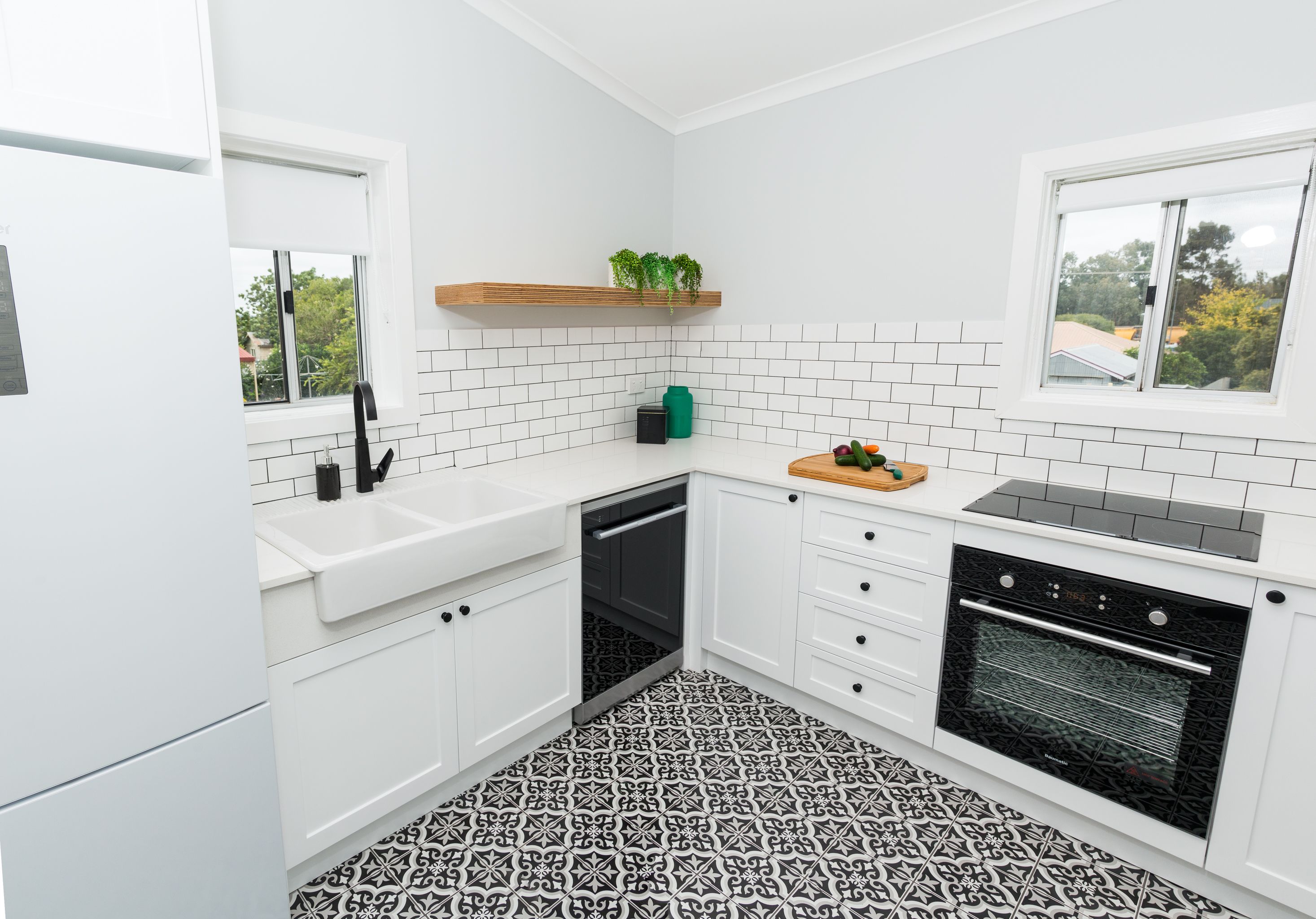 Une cuisine moderne avec des meubles blancs, un carrelage noir et blanc, un four encastré et une fenêtre donnant sur l’extérieur.
