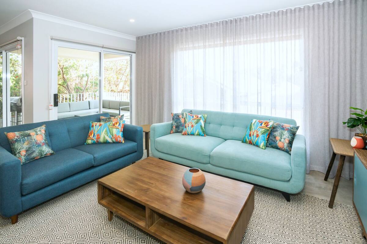 Ein Wohnzimmer mit zwei Sofas, einem Couchtisch und Blick ins Freie durch große Fenster.