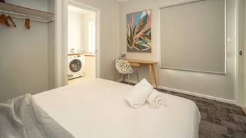 A hotel room with a bed, a desk, a chair, a washing machine, and a painting on the wall.