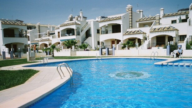 Piscina rodeada por edifícios altos com varandas e céu claro.