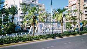 Rua com palmeiras e um edifício com varandas.